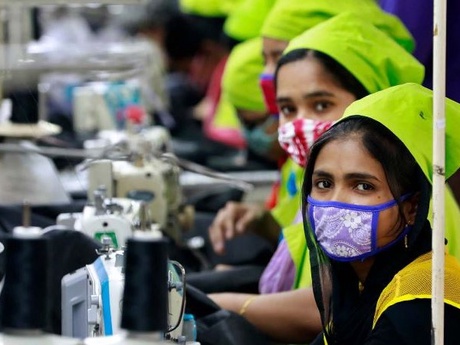 Female Bangladesh garment workers wearing masks using sewing machines inside a factory