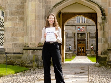 Morgane holding her certificate on campus at Old Aberdeen