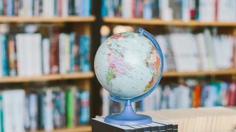 A globe sits on top of a stack of encyclopaedias, in the background are bookshelves