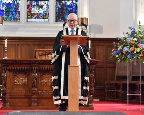 A photograph of Principal George Boyne dressed in robes talking at the podium in King's College Chapel