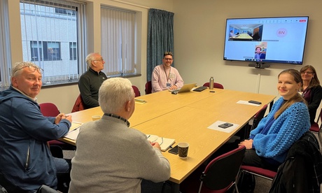 6 people sitting around a table and 1 person on a wall mounted screen to join the discussion.