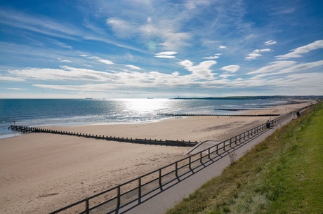 A very sunny day at Aberdeen Beach. The sea is a vibrant blue colour and there are some white clouds streaked across a bright blue sky. The beach has no one on it.