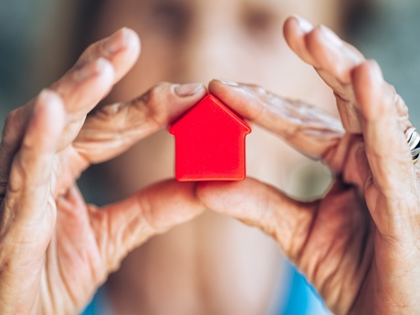 An older woman holding a model of a small red house in her hand