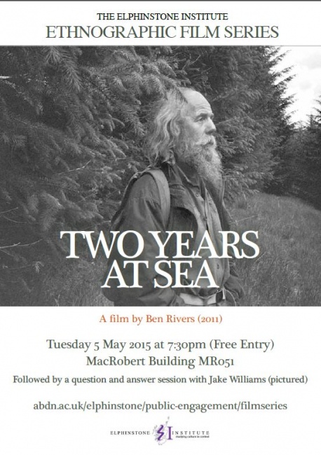 Bearded man stands in front of forest, facing away from the trees