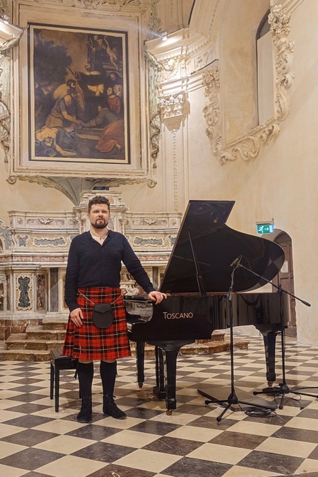 Man in kilt stands next to piano in ornate baroque room