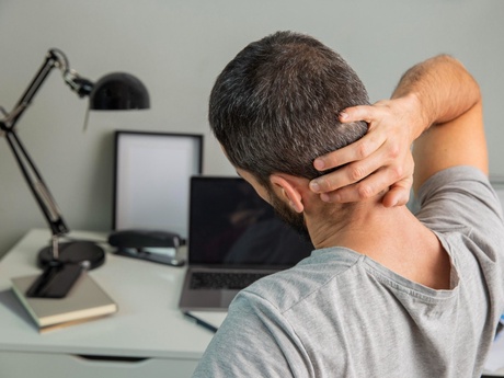 Picture of a man holding his back sitting at a desk.