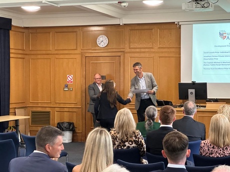 Photograph Alisdair Sutherland presenting the Theresa Hunt Excellence Prize to winner Karolena Brown with Greg Godron in the background.