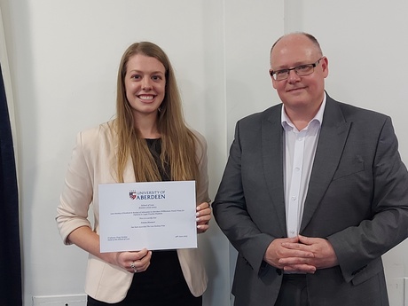 Photograph of Prize winner Emma Stewart, holding their certificate, alongside Head of Law School Prof Greg Gordon