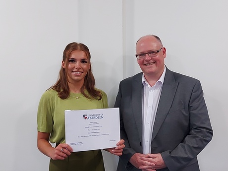 Photograph of Prize winner Georgia McLean, holding their certificate, alongside Head of Law School Prof Greg Gordon