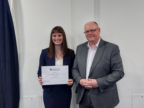 Photograph of Prize winner Hannah McMahon, holding their certificate, alongside Head of Law School Prof Greg Gordon