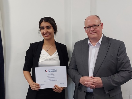 Photograph of Prize winner Melina Otifeh, holding their certificate, alongside Head of Law School Prof Greg Gordon