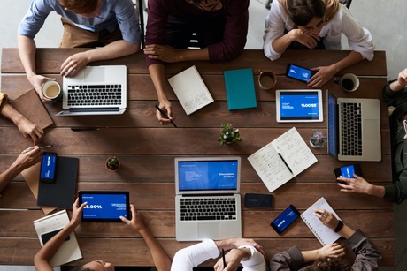 Top view of individuals sitting around a table with laptops and coffee