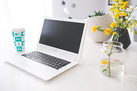 Laptop with a coffee cup and some yellow flowers on a desk