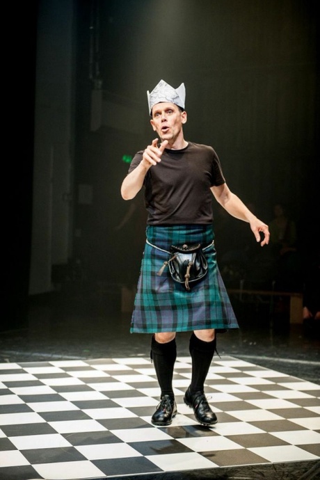 The artist Andy Cannon performing in a dark room wearing a kilt, t-shirt with a crown on his head.