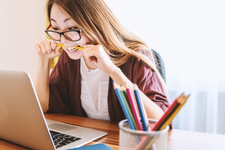 Young woman looking at a laptop biting a pencil