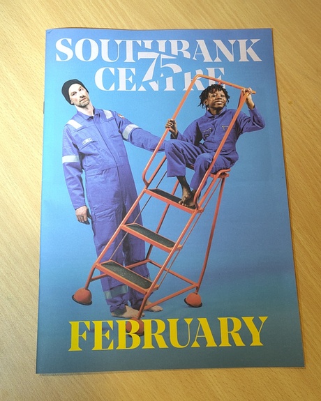 Cover for the February Edition of Southbank Centre, featuring two people in blue jumpsuits, on an orange ladder, in front of a blue background.