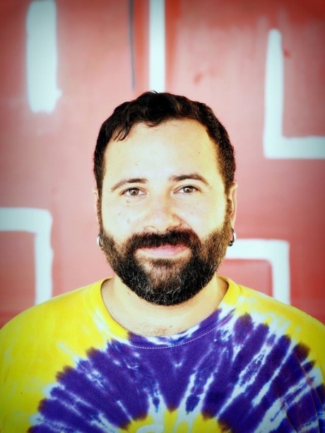 Dr Luis Manuel Garcia Mispireta, in a tie-die T-shirt, in front of a red wall with lights on it.