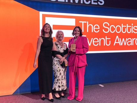 Three women on the stage holding the trophy