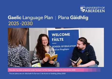 Two people holding Gaelic books with a Gaelic sign that says 'Welcome' on it