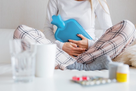 Woman holding a hot water bottle surrounded by medications