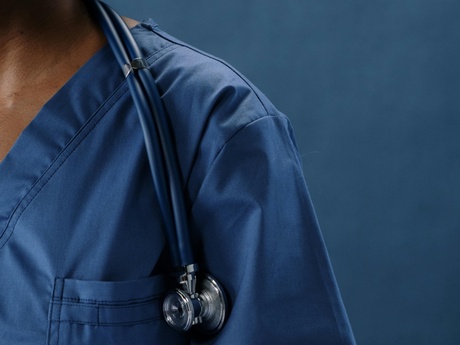 The shoulder of a surgeon in blue scrubs with a stethoscope round their neck