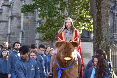 A person sat on top of a bull mascot being carried aloft