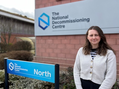 A woman with dark hair standing by a sign for the National Decommissioning Centre