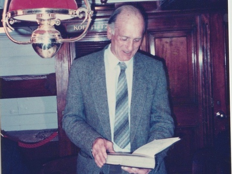 A smiling man in a grey suit holding a book