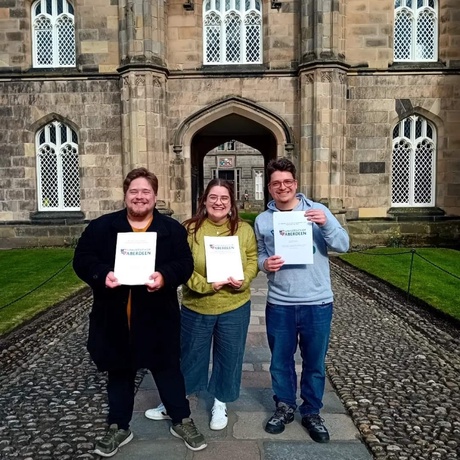 Josh (left), Anna (centre) and John (right) holding their dissertations on campus