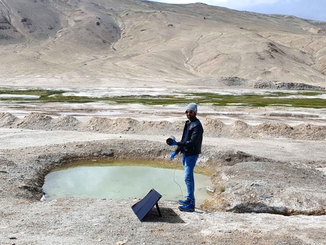 A man standing beside a large puddle of water holding scientific equipment