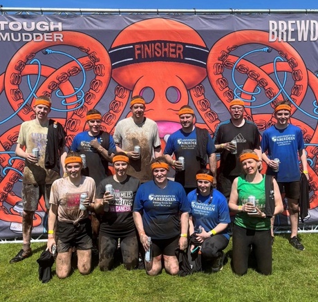 Team Tranquility at Tough Mudder: 11 people posing in front of a large Tough Mudder poster