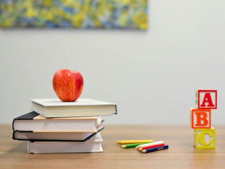 A desk with a pile of books, an apple and some ABC building blocks