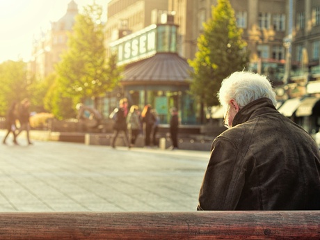 A man sits alone on a bench in a crowded plaza