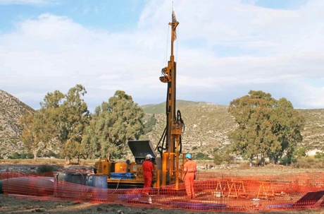 A large piece of industrial equipment flanked by two people in boiler suits and hard hats in the countryside