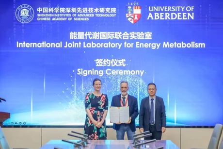 Three people posing in front of a digital screen holding an official document