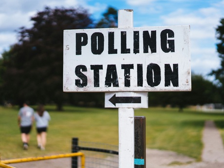 A pollingstation sign in an urban area with a couple walking behind it