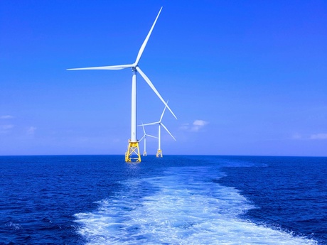 An offshore windfarm as viewed from a boat on the water, with blue sky in the background