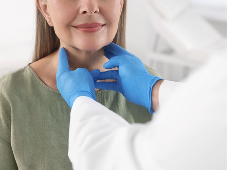 A doctor in surgical gloves examining a female patient's neck