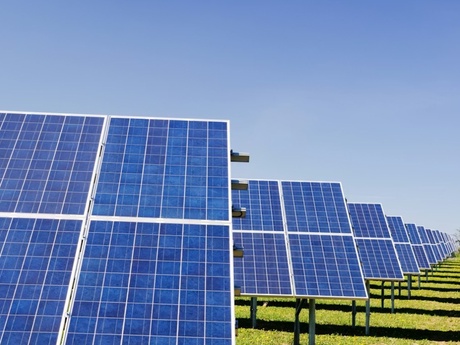 A line of solar panels in a field with blue sky in the background