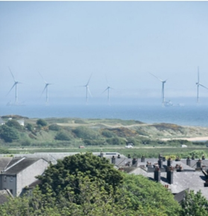 Offshore wind turbines off the North East coast of Scotland, seen beyond rooftops and sand dunes. The turbines contribute to the region&rsquo;s renewable energy production.
