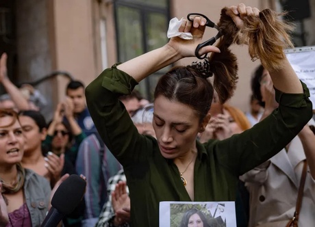 A woman in front of a crowd of protesters, cutting her hair with a paur of scissors.