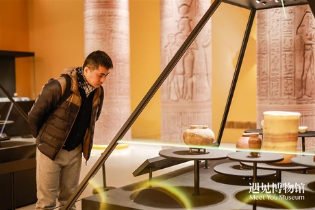 A visitor examines pottery vessels in a pyramid-shaped cabinet with Egyptian temple-like pillars and decor in the background.