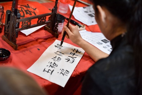 A woman doing Chinese calligraphy in black ink on red canvas