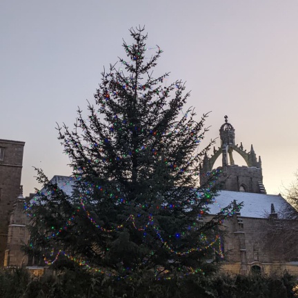 A Christmas tree with lights against a snowy King's College Chapel