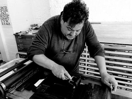 A black and white photograph of Nuno Sacramento screenprinting in a studio