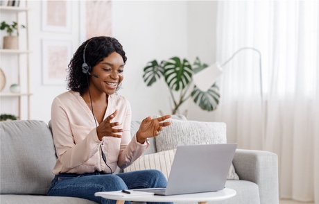 Woman sits on couch with headset on smiling and talking to a camera in a bright white room