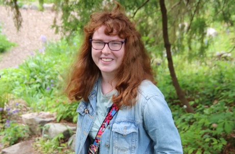 Student with curly long hair and glasses smiling towards camera