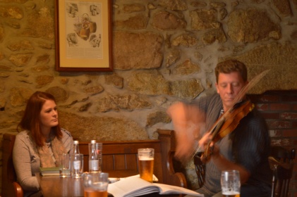 Woman and man sitting at table while man plays fiddle