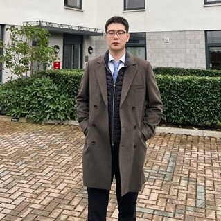 Weihao stands in a long coat in front of a building