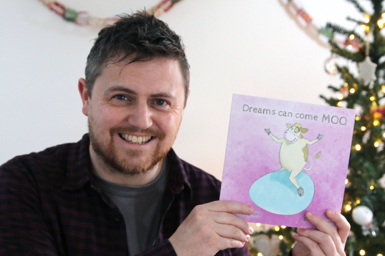 Euan Wemyss holding a copy of the "Dreams can come MOO" book